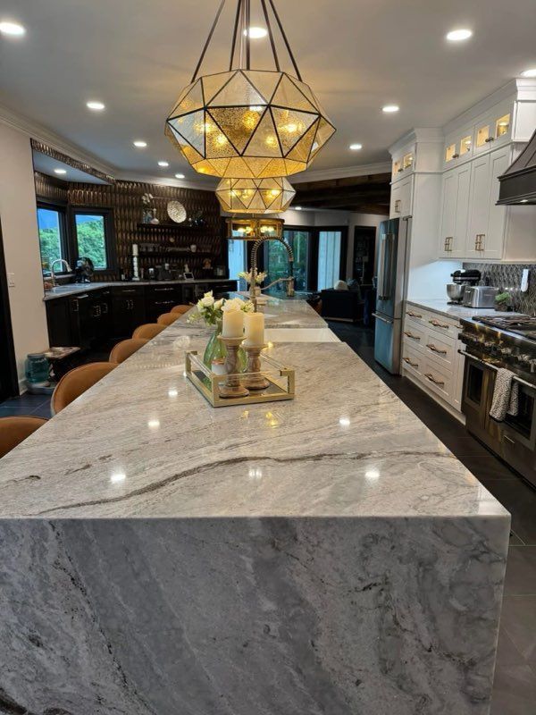 Modern kitchen with large marble island, geometric pendant light, and dark cabinetry