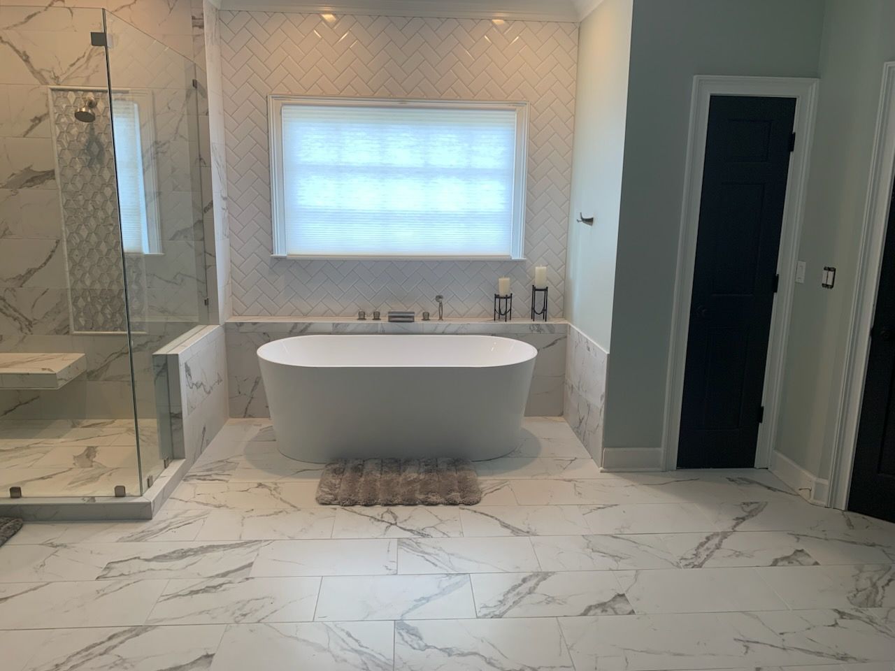 Modern bathroom with freestanding tub, glass shower, marble tile, and a backlit window panel.