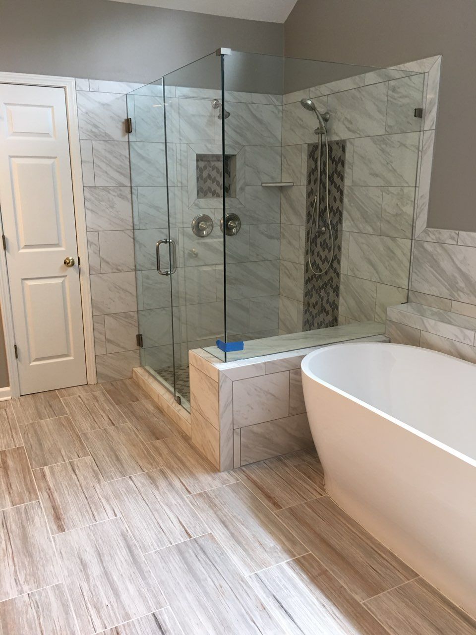 Modern bathroom with glass shower, tiled walls, and freestanding tub on wood-look floor