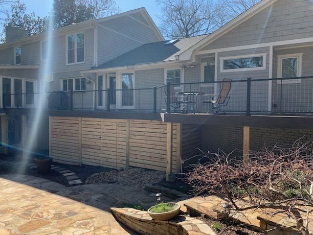 Backyard deck with black railing and patio chairs beside a tan house on a sunny day