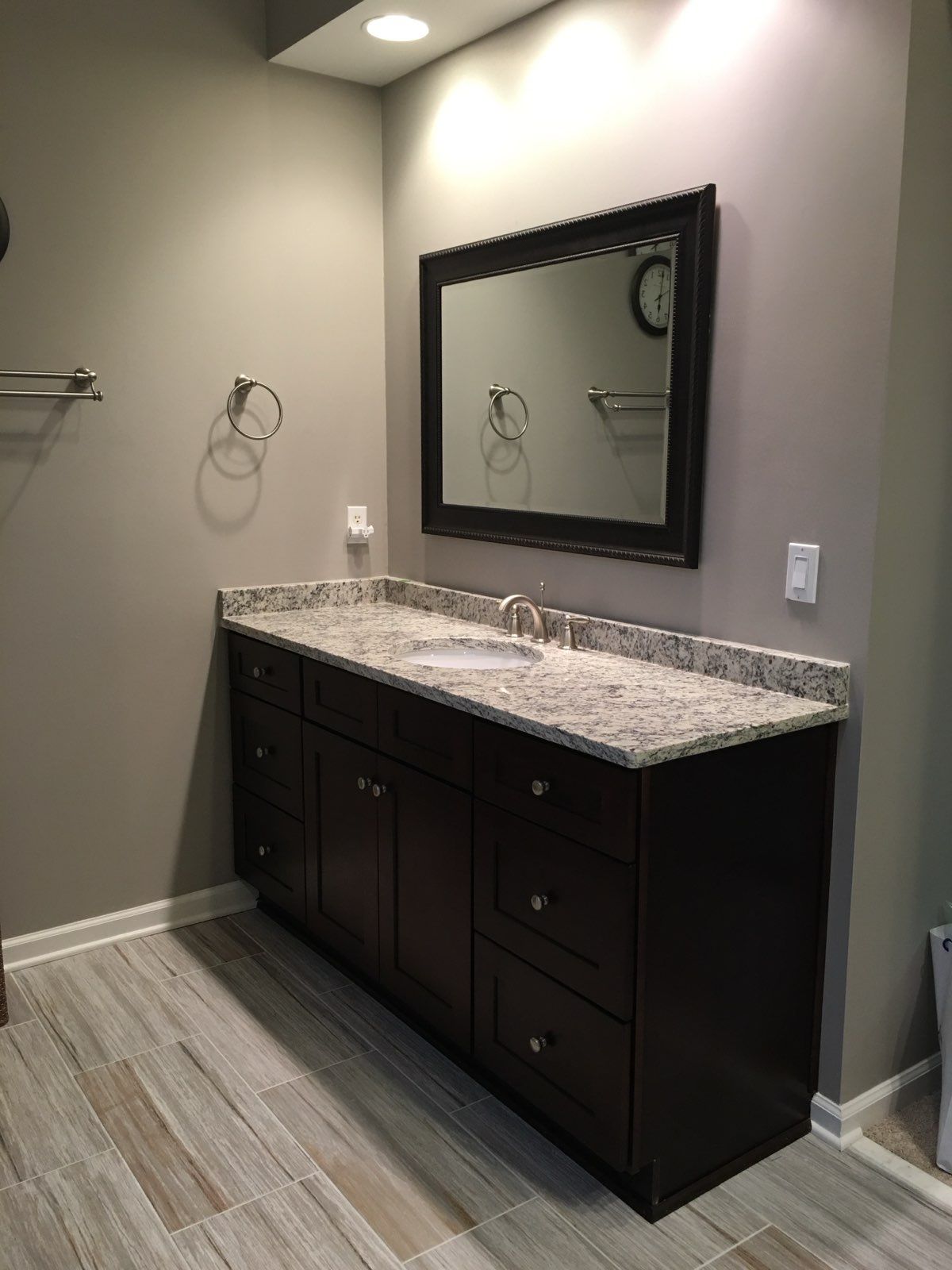 Modern bathroom vanity with dark cabinets, granite countertop, and framed mirror against beige walls.