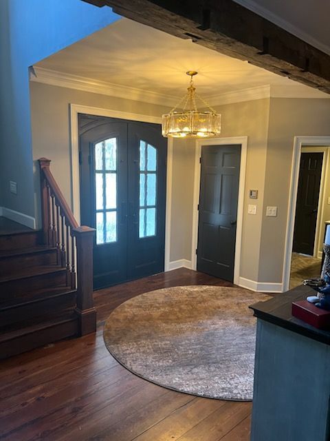 Entryway with dark French doors, chandelier, round rug, and hardwood floors