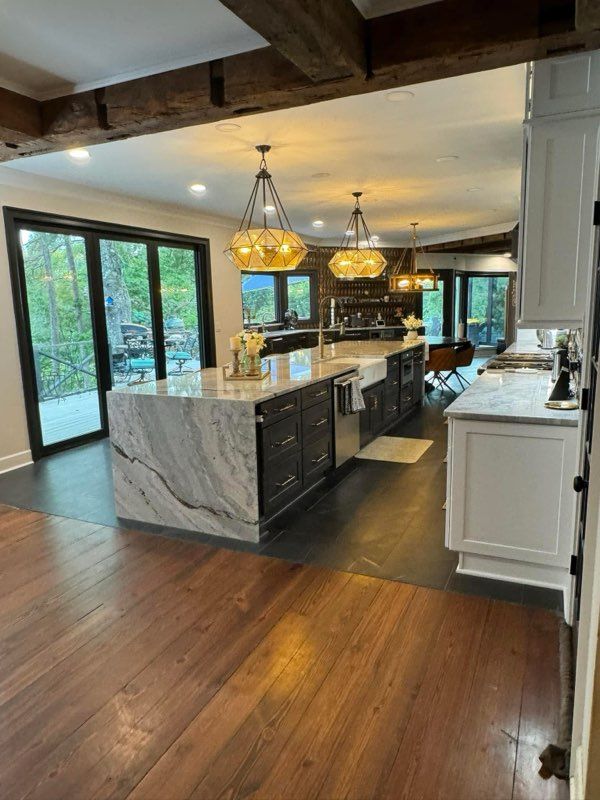 Modern kitchen with marble island, pendant lights, dark cabinets, and hardwood floors opening to a deck.