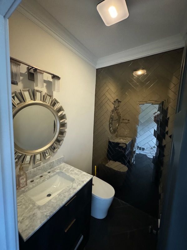 Small bathroom with marble vanity, round mirror, white toilet, and dark tiled shower.