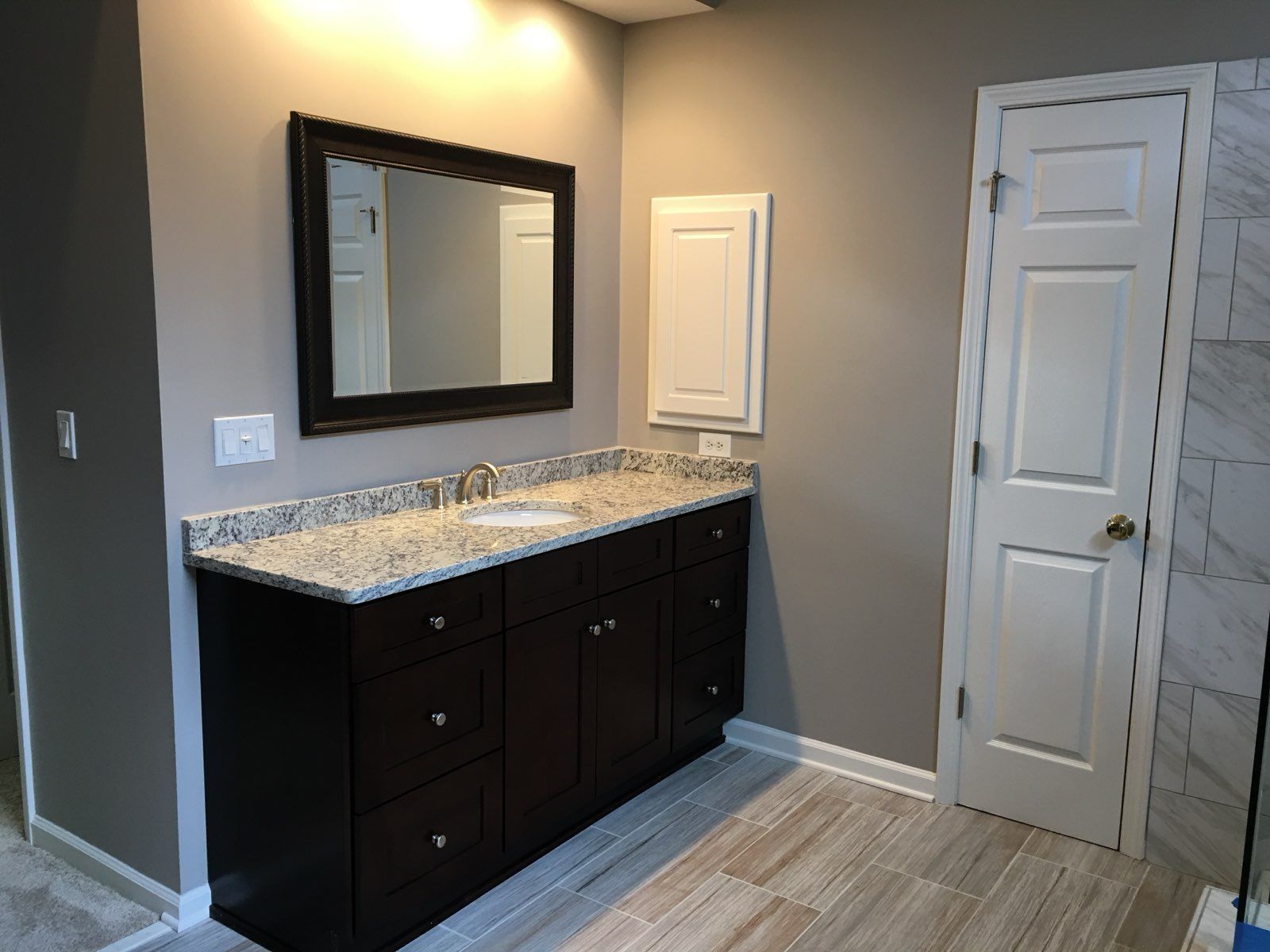 Bathroom vanity with dark cabinets, granite countertop, mirror, and white door in a gray room