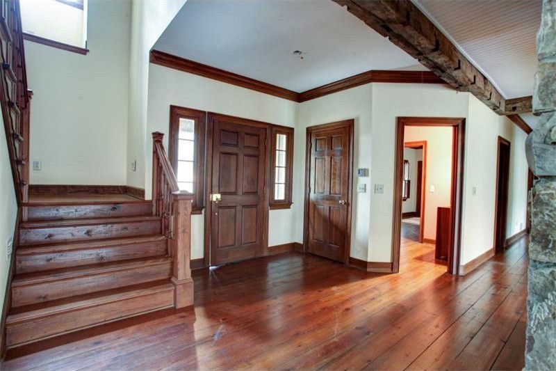 Spacious empty foyer with wooden floors, staircase, and multiple doorways