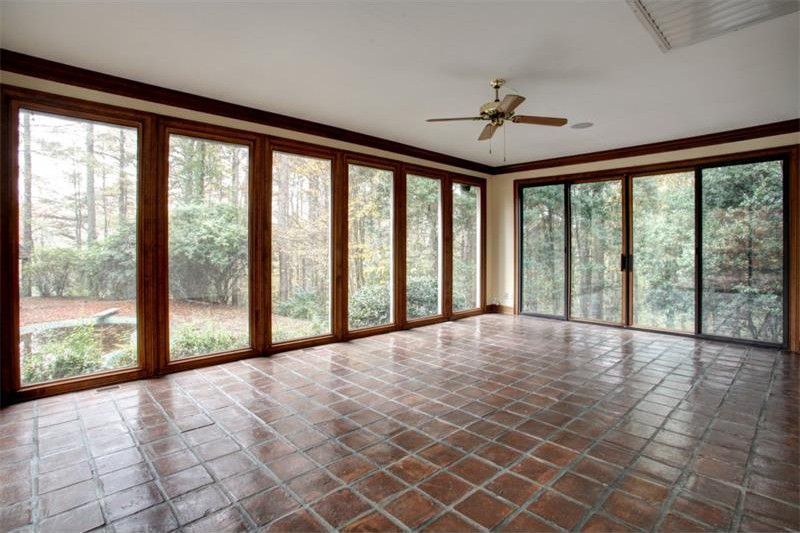 Empty sunroom with wood-framed glass doors, tiled floor, and forest views.