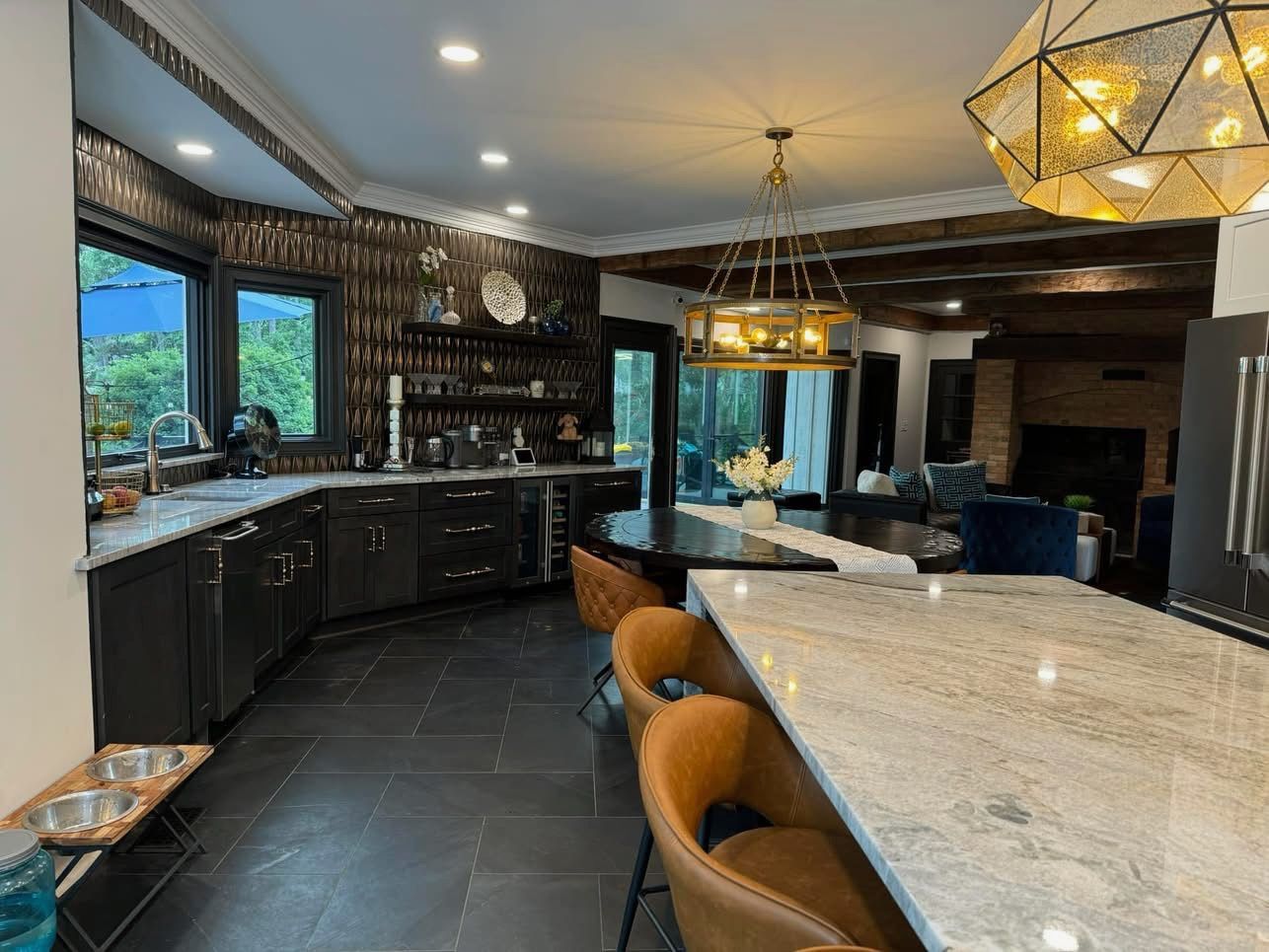 Modern kitchen with dark cabinets, marble island, pendant lights, and blue seating by large windows