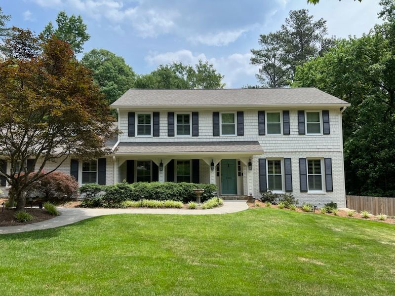 Two-story white suburban house with green shutters, front porch, and a large lawn