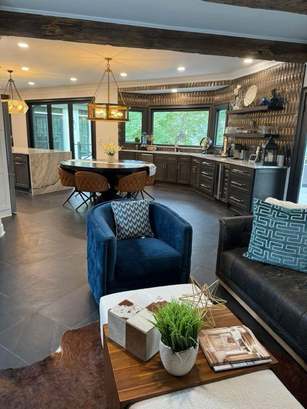 Modern open-plan kitchen and living area with blue chairs, dark cabinetry, and large windows