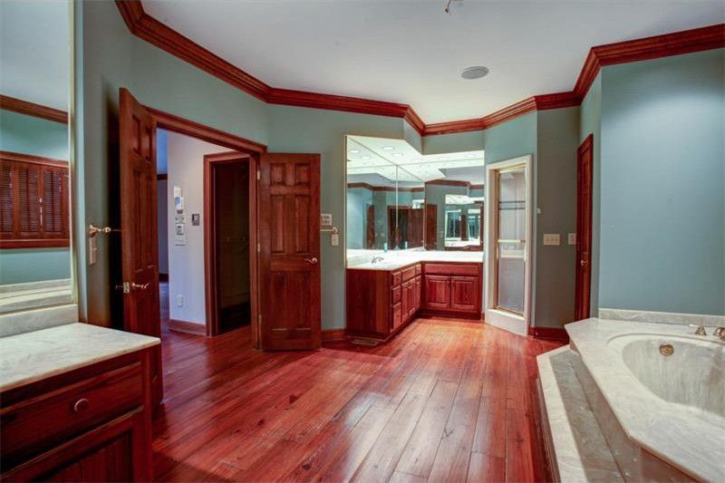 Spacious bathroom with wood cabinets, a soaking tub, large mirror, and polished hardwood floors.