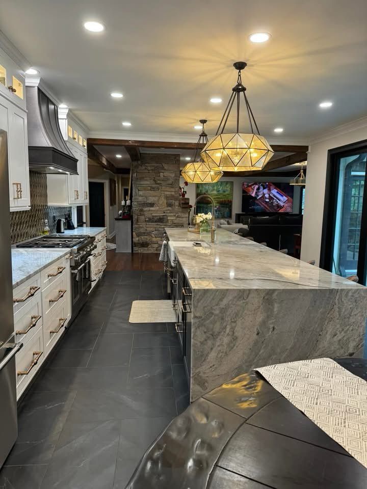 Modern kitchen with marble island, pendant lights, dark floor, and stone fireplace backdrop