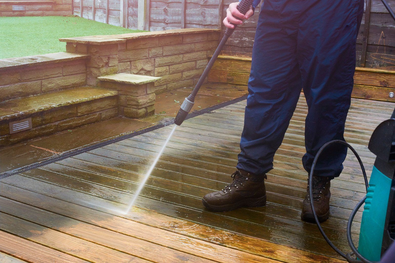 A man is using a high pressure washer to clean a wooden deck.