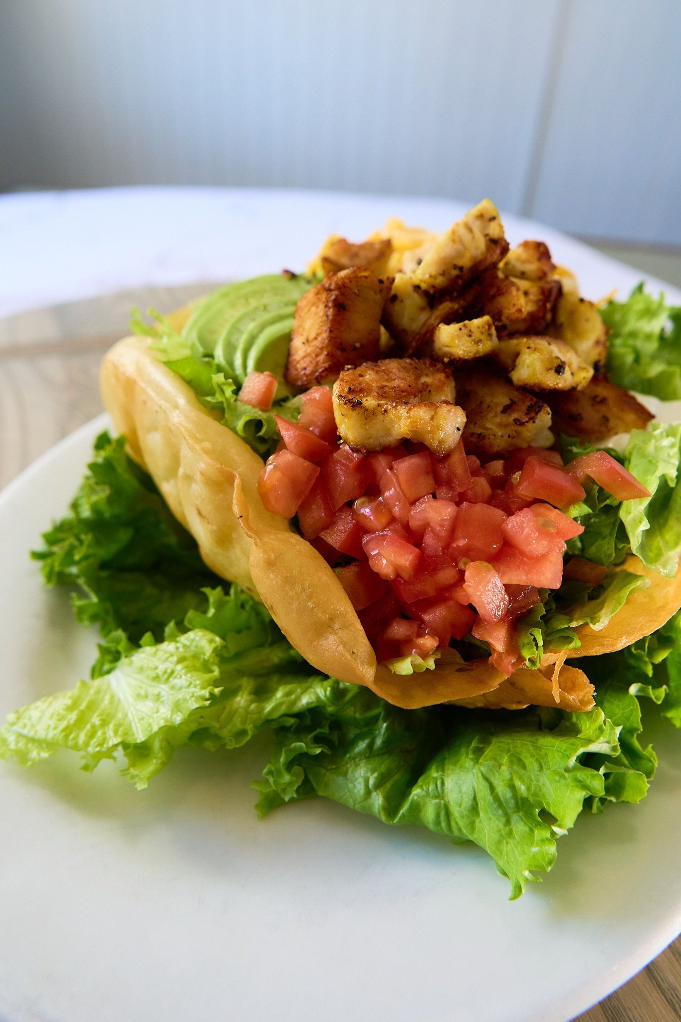 A close up of a taco with lettuce , tomatoes and avocado on a plate.