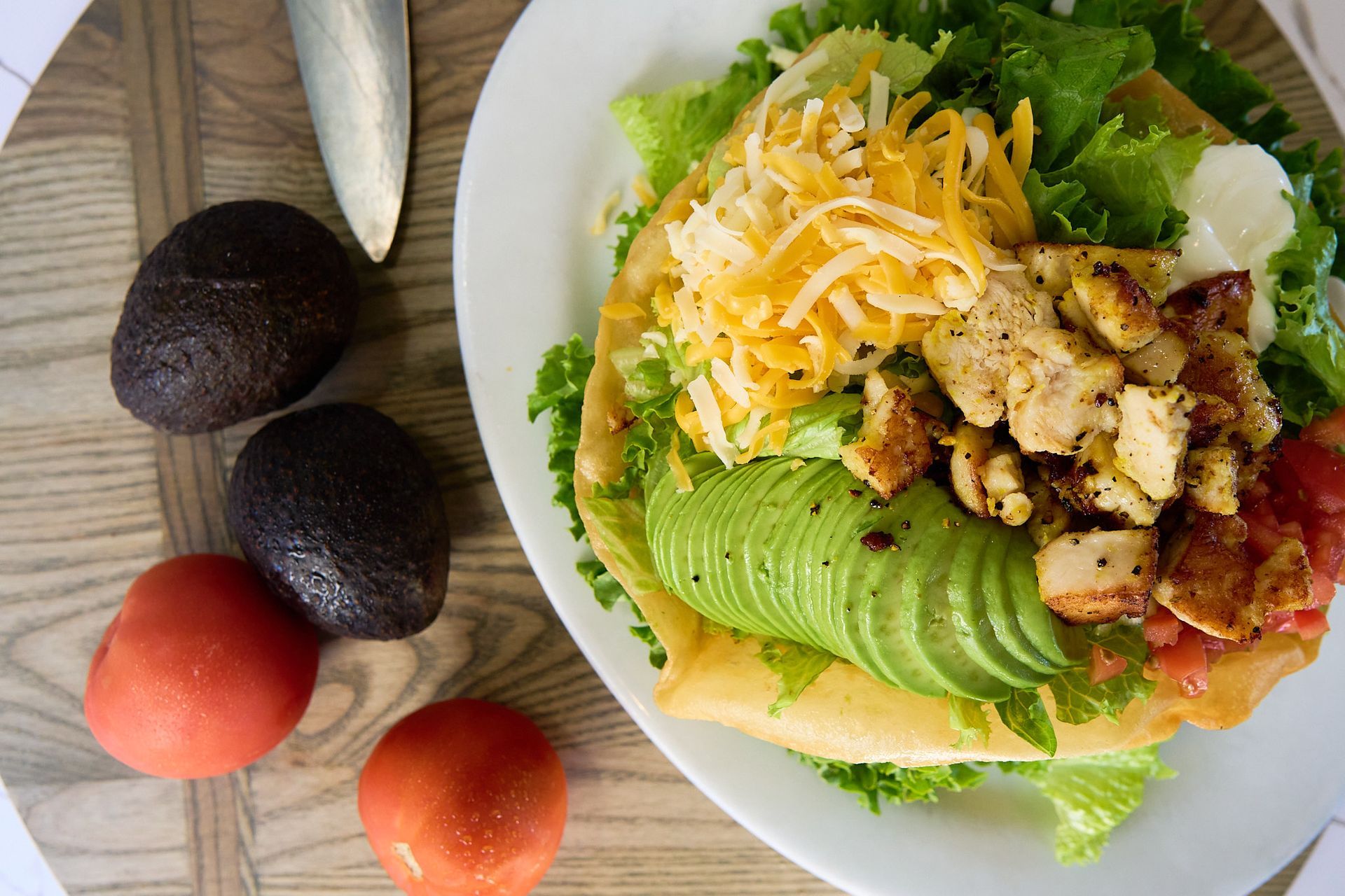 A plate of food with avocado , cheese , tomatoes and lettuce on a wooden table.