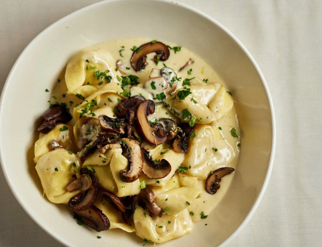 A white bowl filled with pasta and mushrooms on a table.