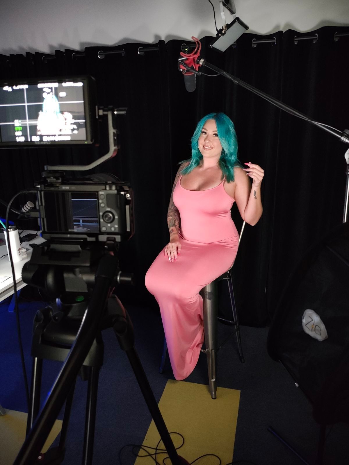 A woman in a pink dress is sitting in front of a camera.