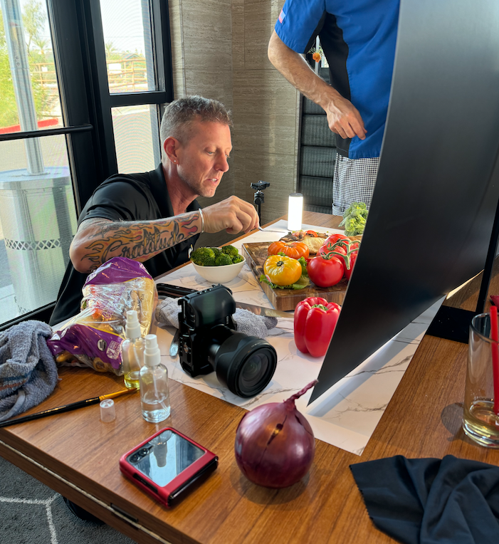 A man is sitting at a table with vegetables and looking at a computer screen
