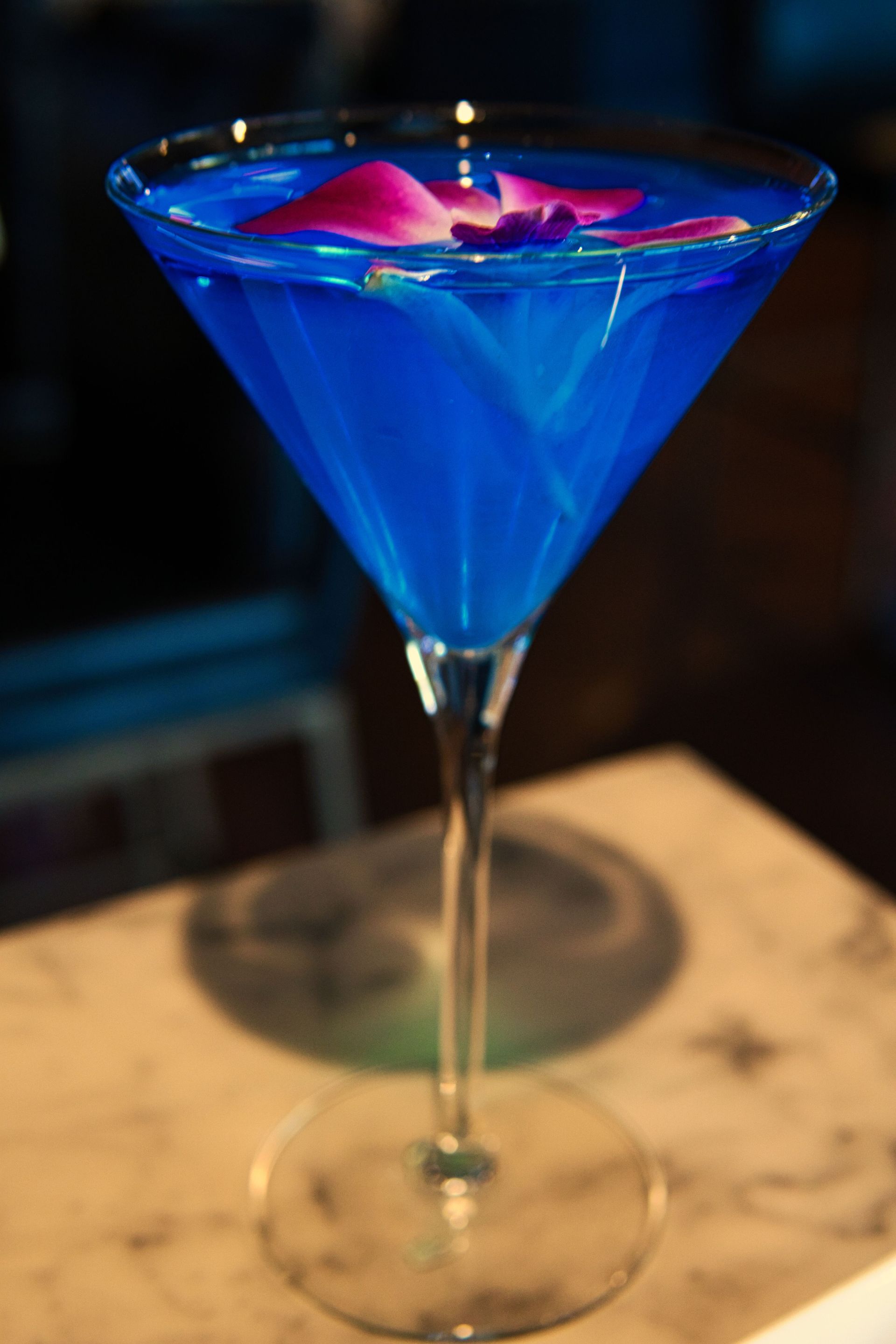 A blue martini with a pink flower in it