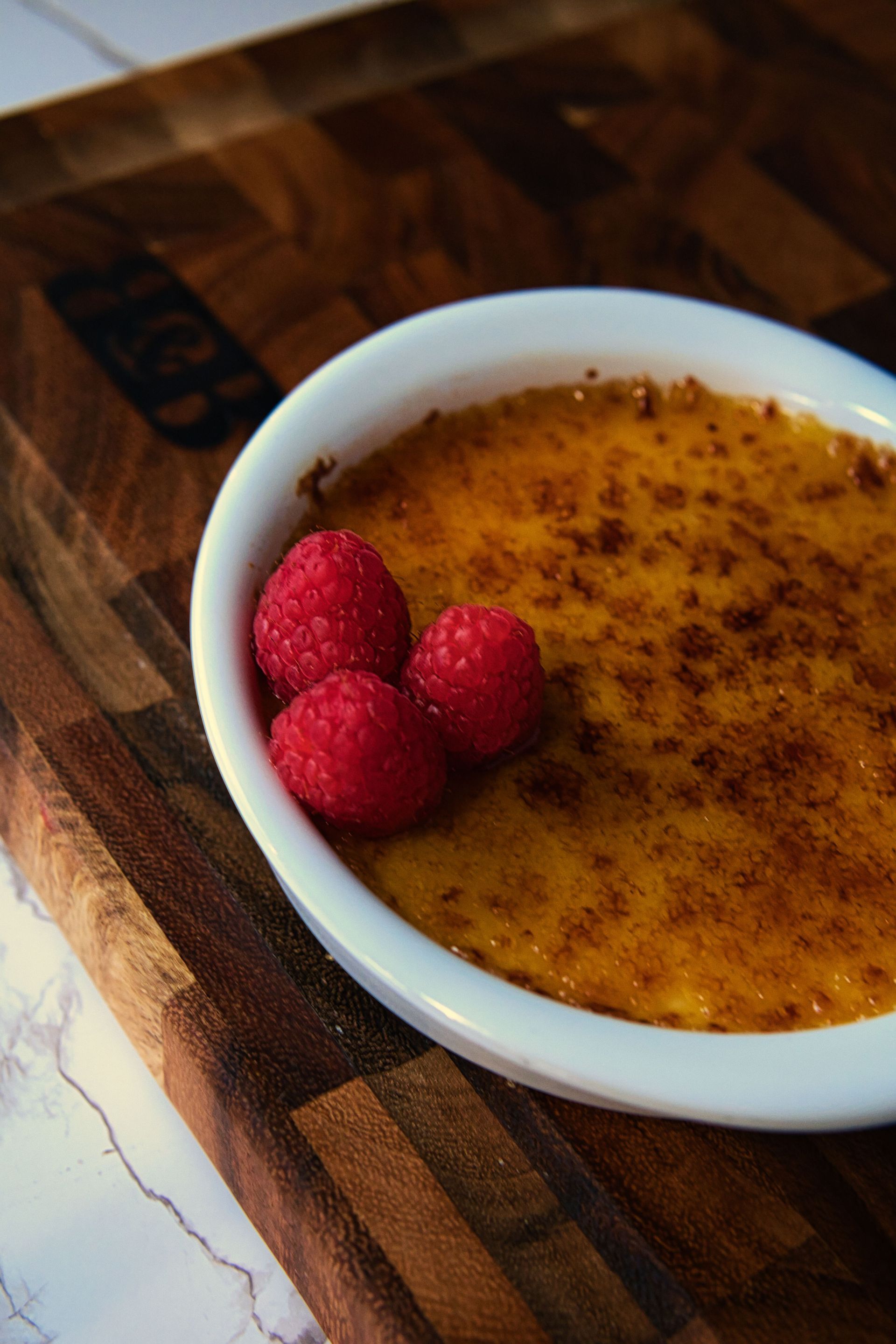 A bowl of food with raspberries on top is on a wooden cutting board.