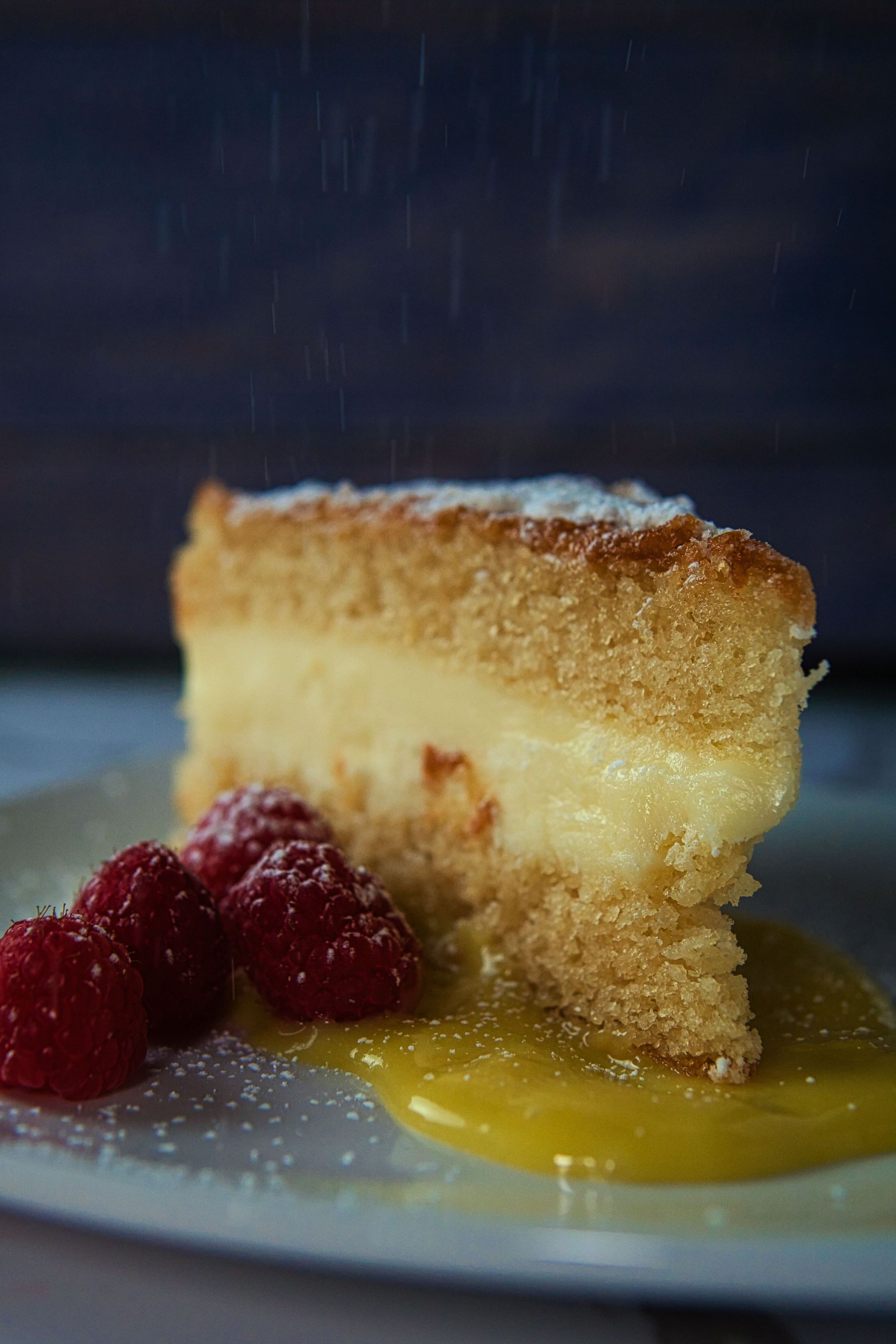 A slice of cake with raspberries and lemon sauce on a plate.