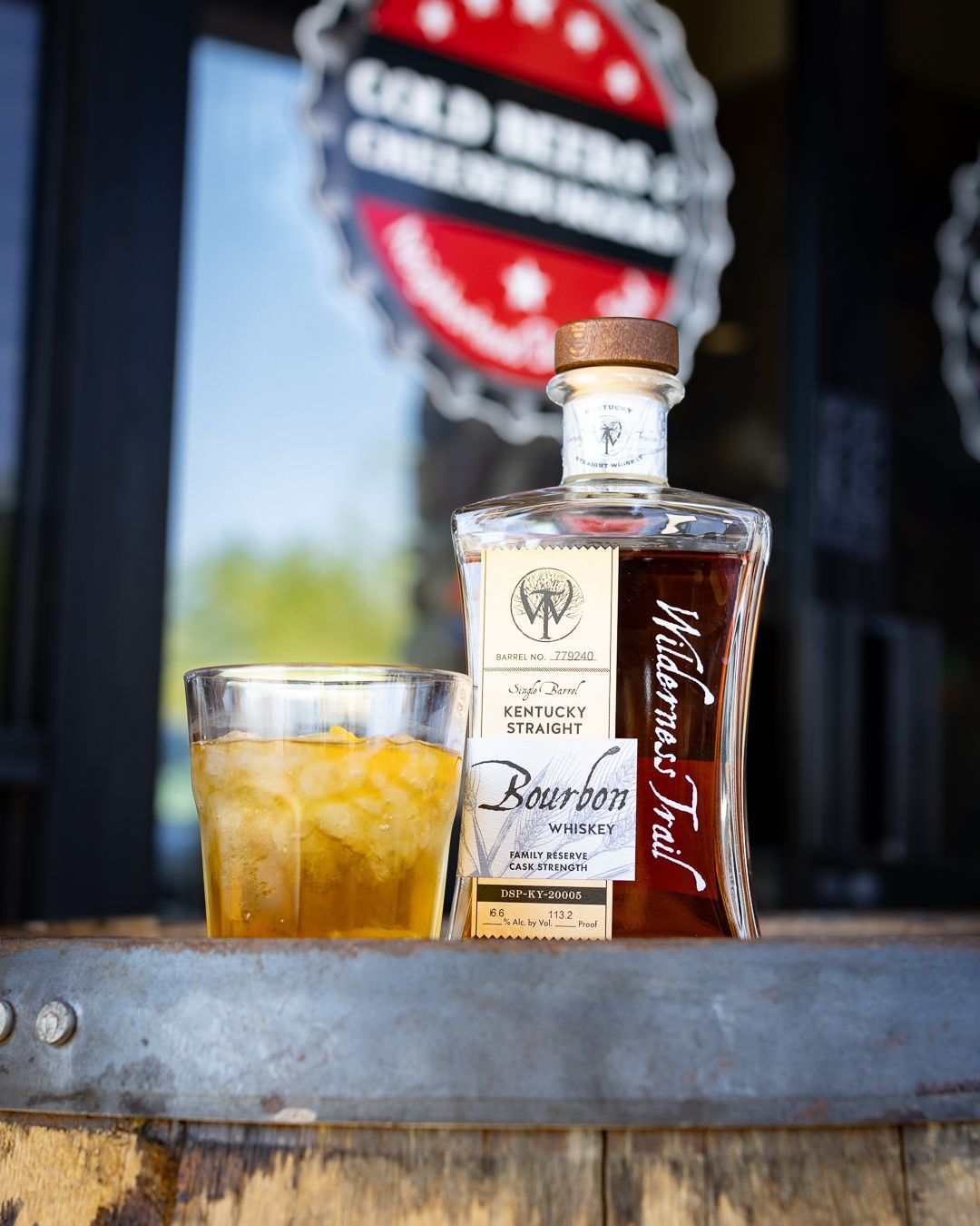 A bottle of whiskey and a glass of whiskey are on a wooden barrel.