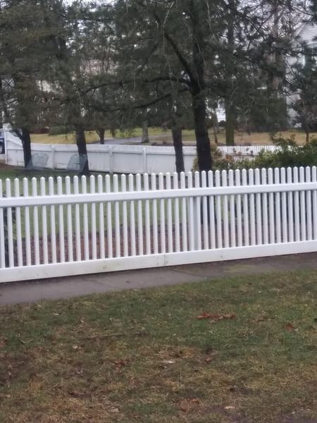 A white picket fence is surrounded by grass and trees.