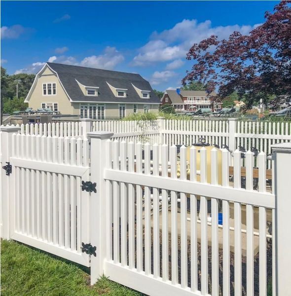 A white picket fence surrounds a swimming pool in front of a house.