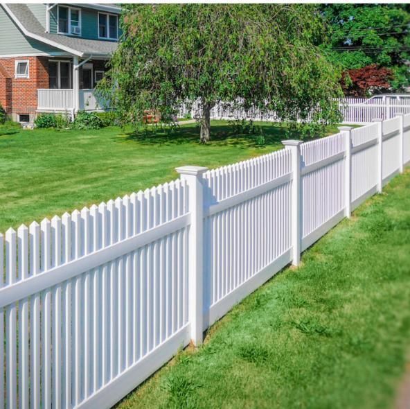A white picket fence surrounds a lush green yard in front of a house.