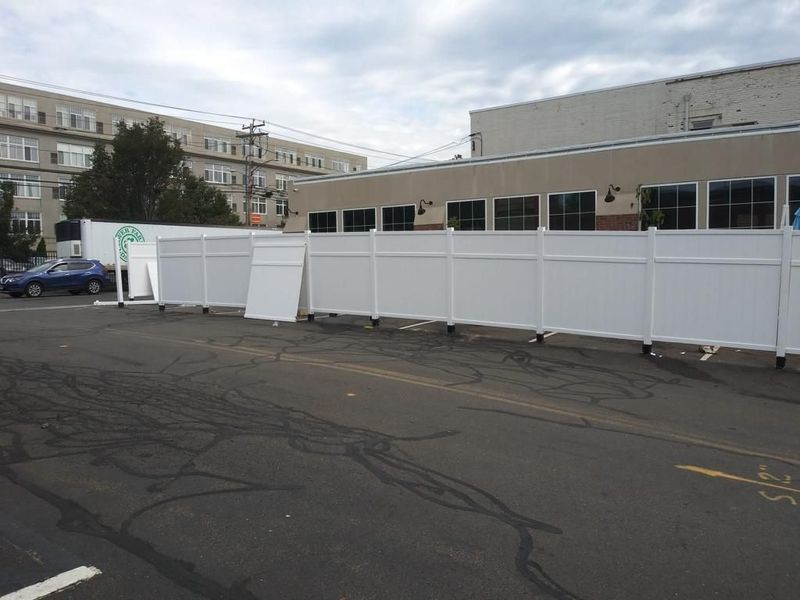 A white fence is surrounding a parking lot in front of a building.
