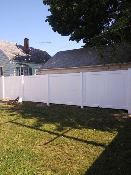 A white fence surrounds a lush green yard in front of a house.