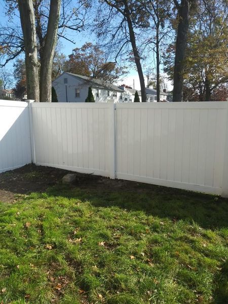 A white fence surrounds a lush green yard with trees in the background.