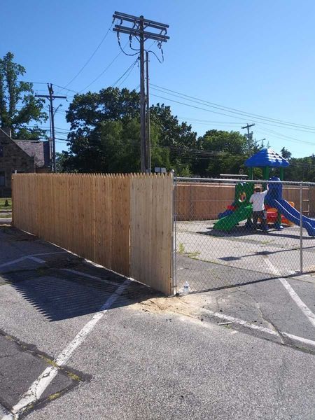 A wooden fence surrounds a playground in a parking lot