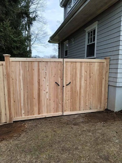 Wooden double gate in front of a gray house, with black handles.