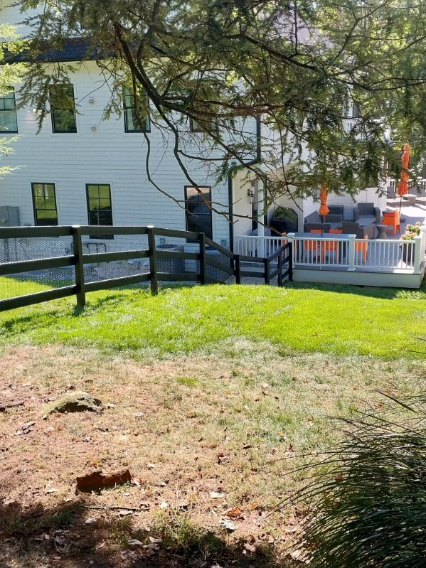 Backyard with white house, wooden deck, green grass, and a black fence.