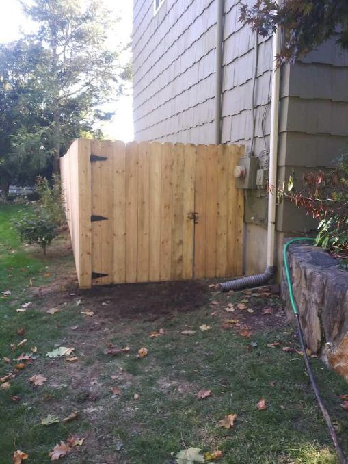 Wooden fence against a house, covering utility area. Green grass and leaves.