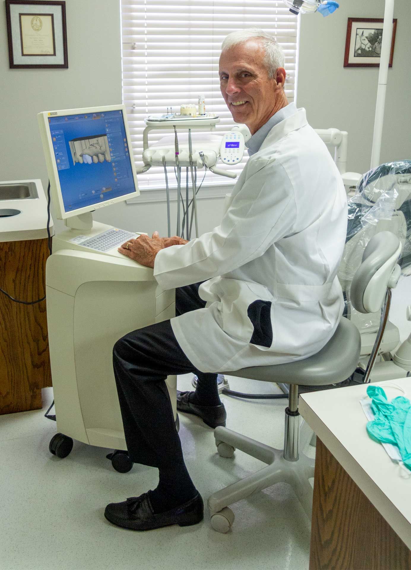 A dentist is sitting in front of a computer in a dental office.