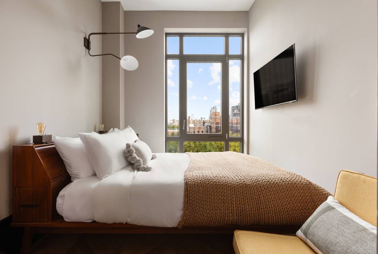 Bedroom with bed, window, TV, and modern lighting. Neutral colors.