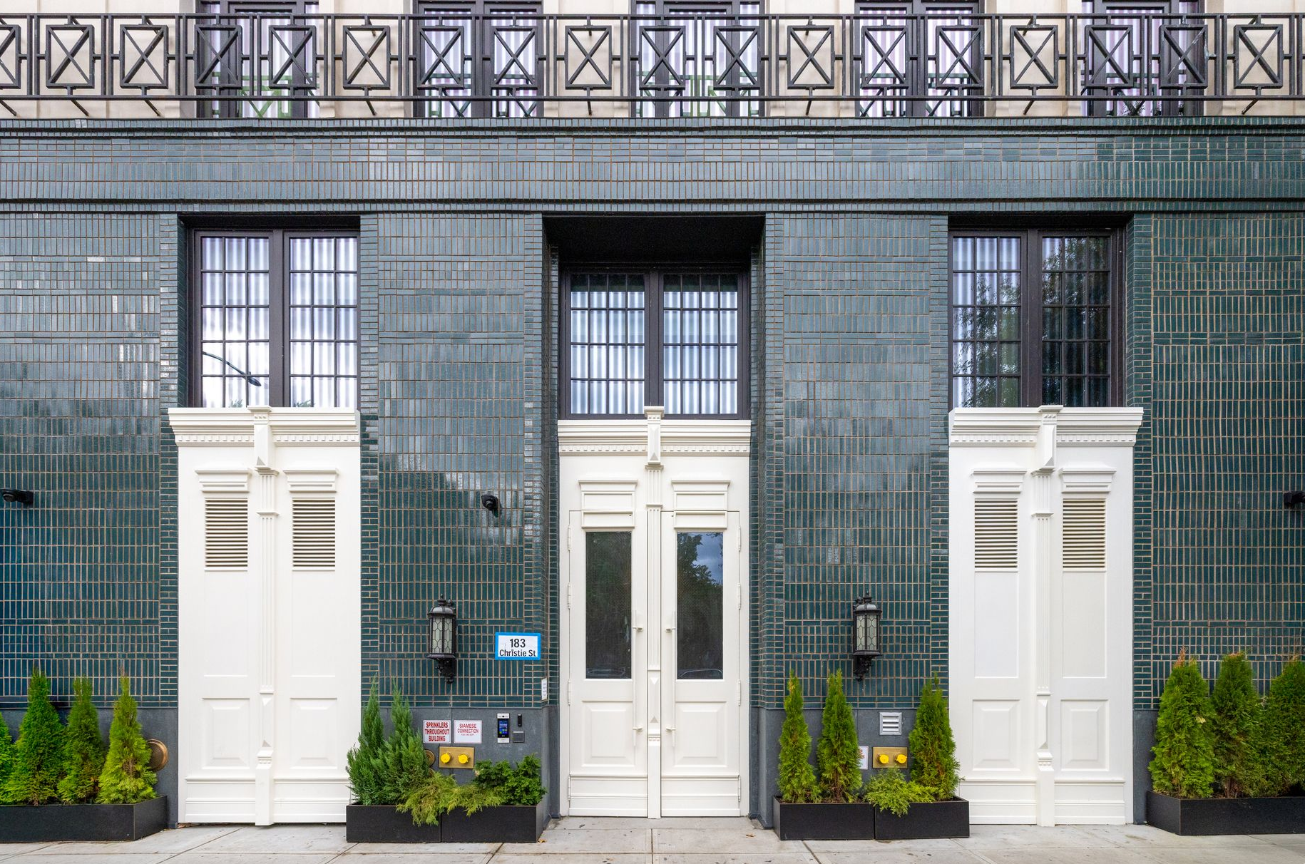 Building facade with teal tile, white doors and trim, black ironwork balcony.