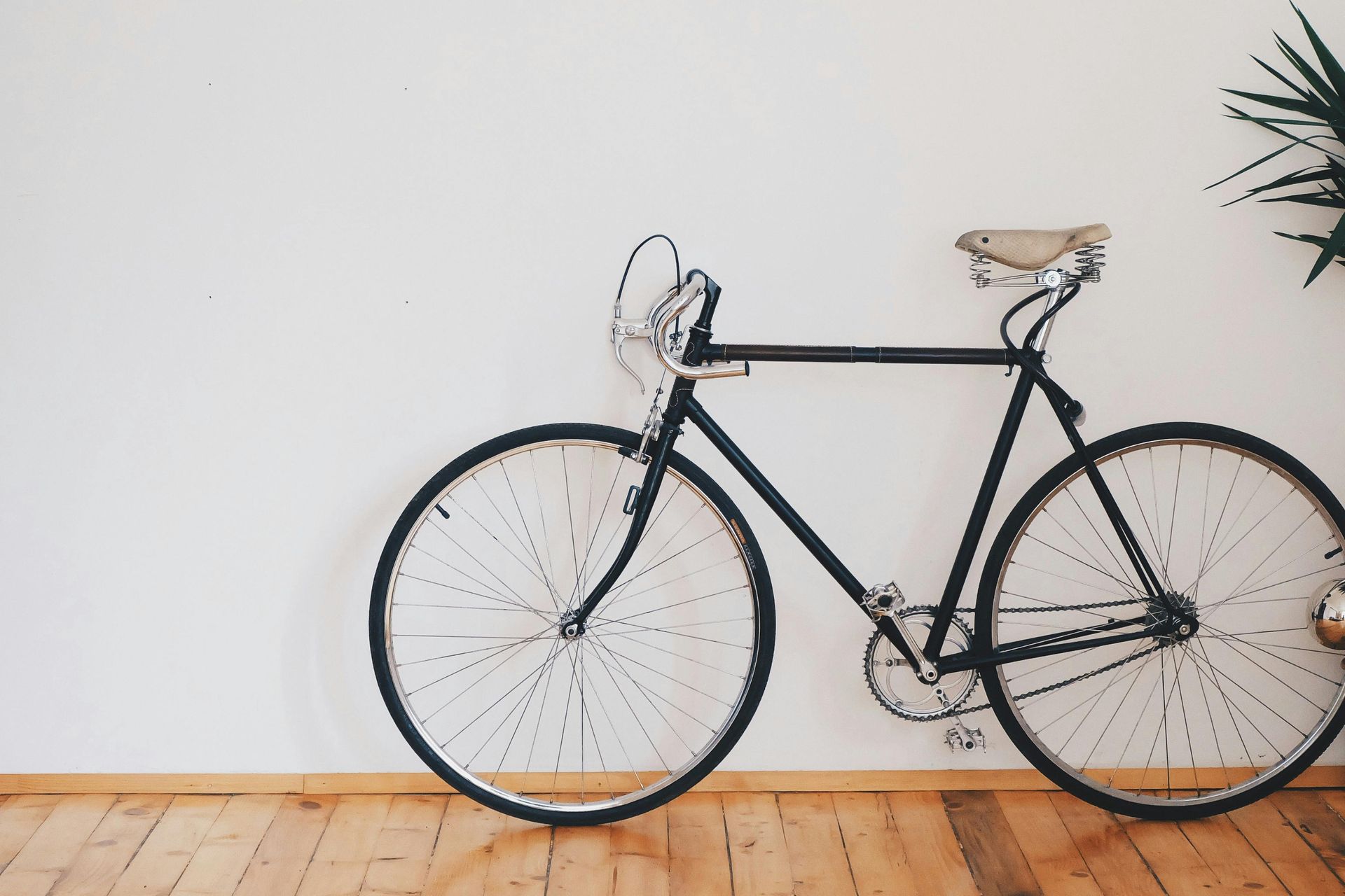 Black bicycle against a white wall and wooden floor.