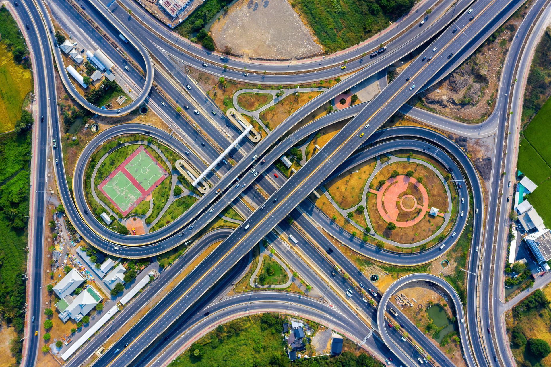 An aerial view of a highway intersection with a tennis court in the middle.