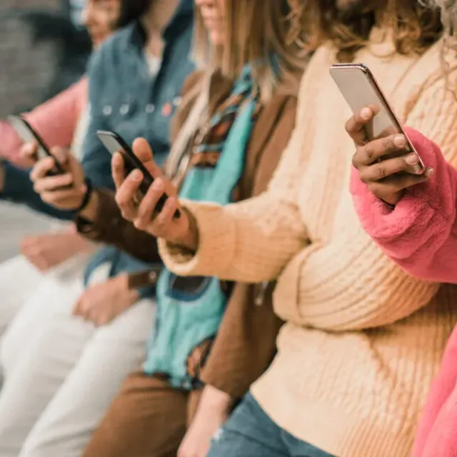 A group of people are sitting in a row looking at their phones.