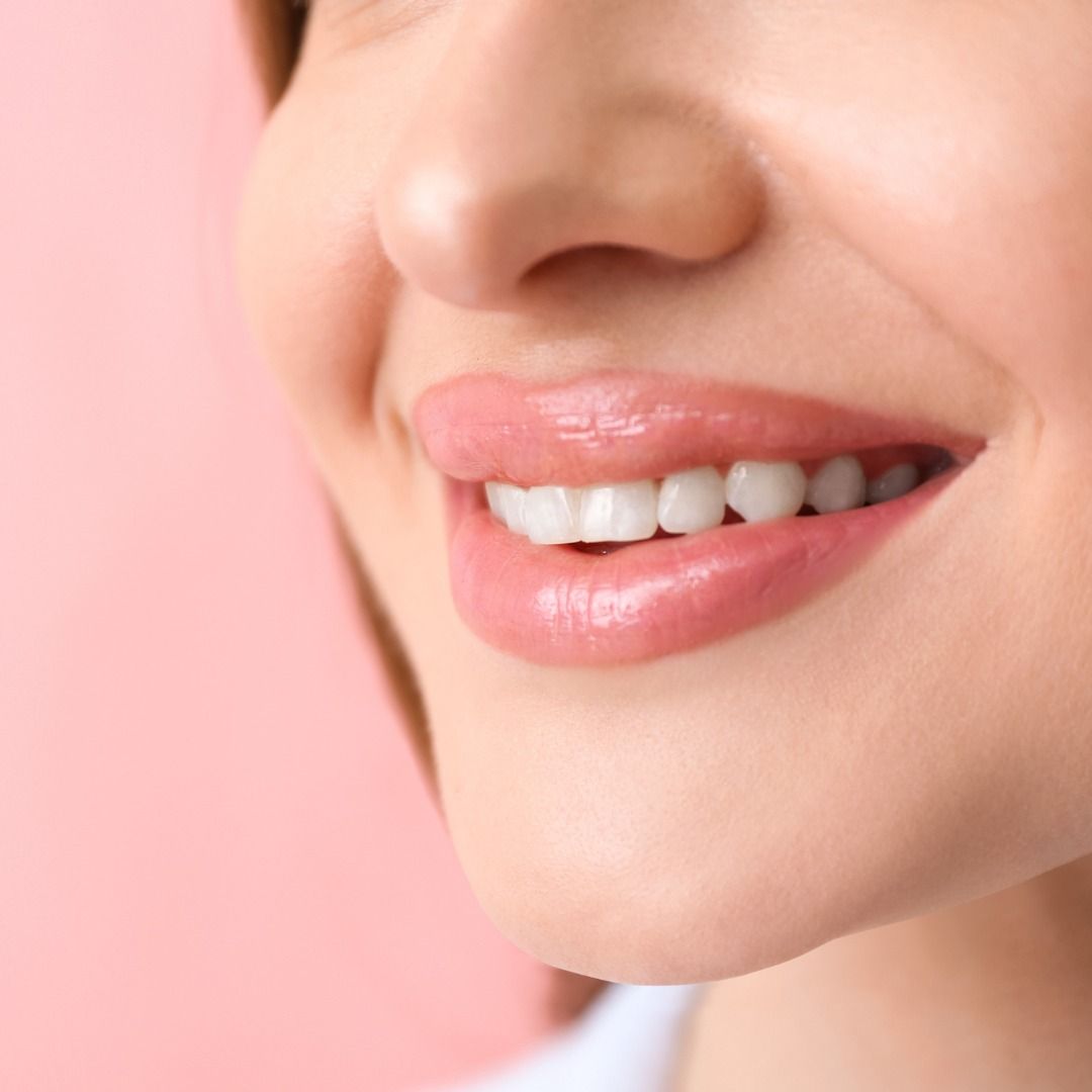 Close-up of smiling lips with glossy pink lipstick on a soft pink background