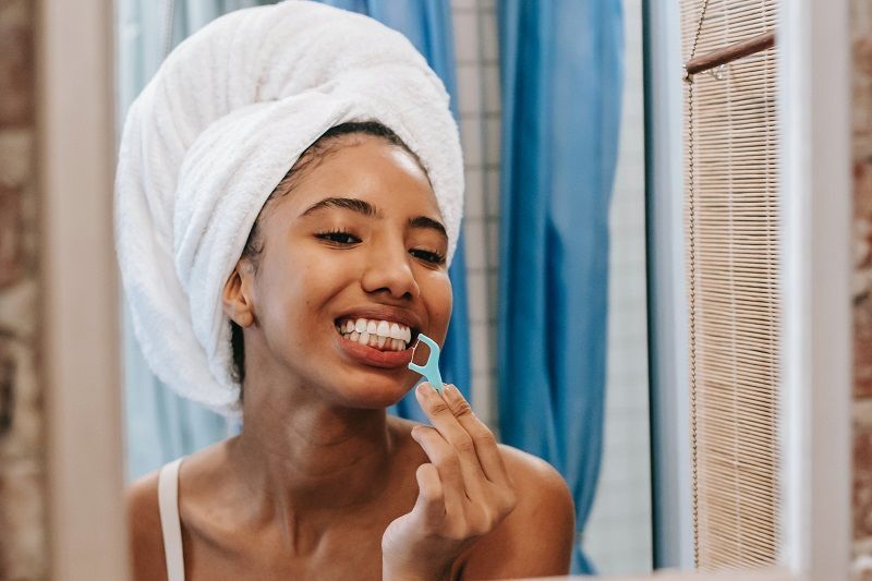 Woman in a towel brushing her teeth in a bathroom mirror