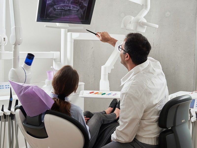 Dentist showing an X-ray on a monitor to a seated patient in a dental clinic