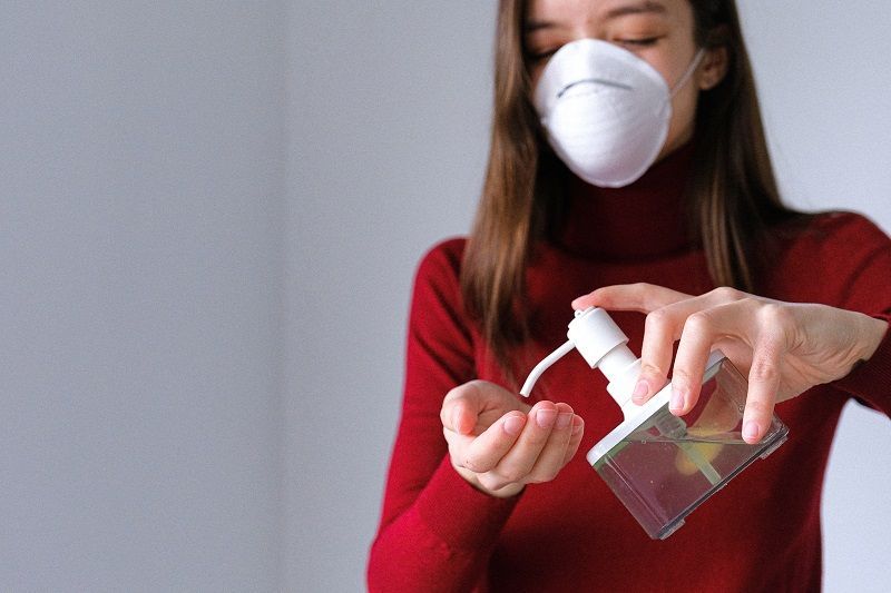 Person in a red sweater wearing a mask and using hand sanitizer from a bottle