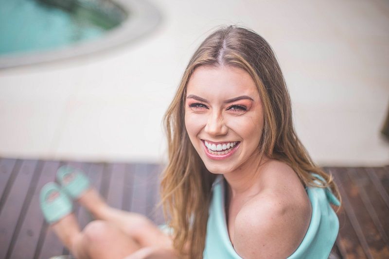 Smiling woman in a light blue top sitting outdoors, holding a smartphone