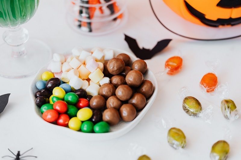 Assorted colorful candies in a white bowl on a festive table with Halloween decorations