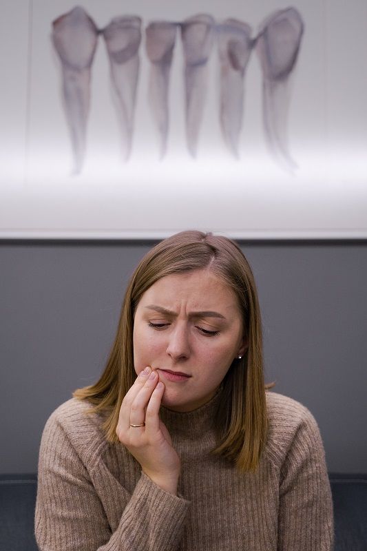 Woman holding her cheek in pain, with a blurred image of teeth in the background.