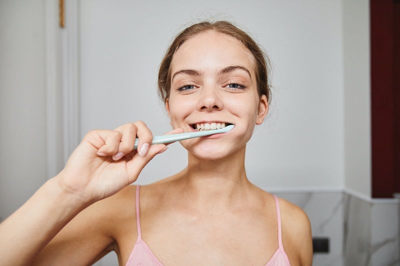 Smiling woman brushing her teeth in a bathroom mirror